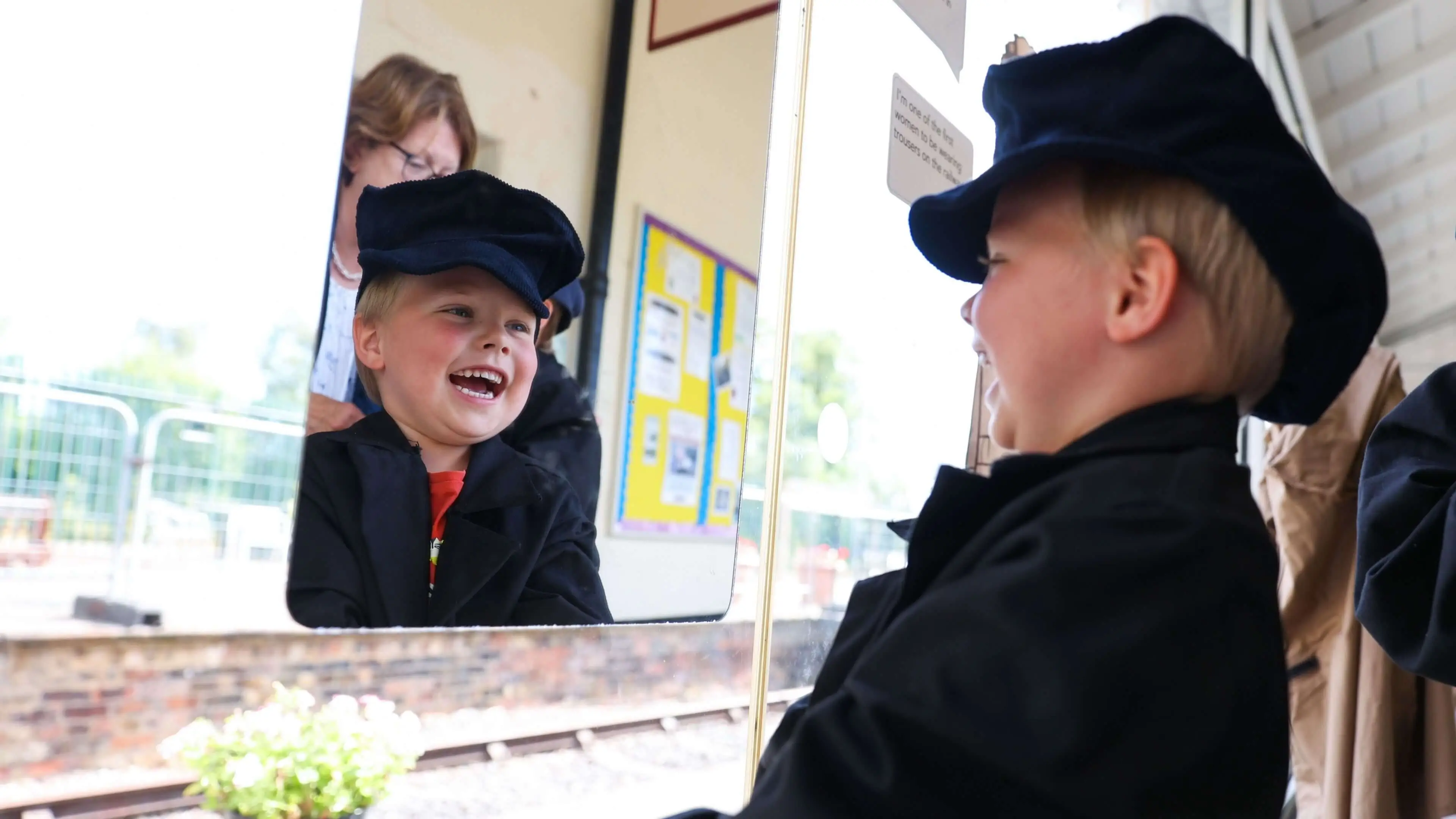 Photo of a boy looking in a mirror and smiling at his own reflection. He is wearing an old railway flat cap. 