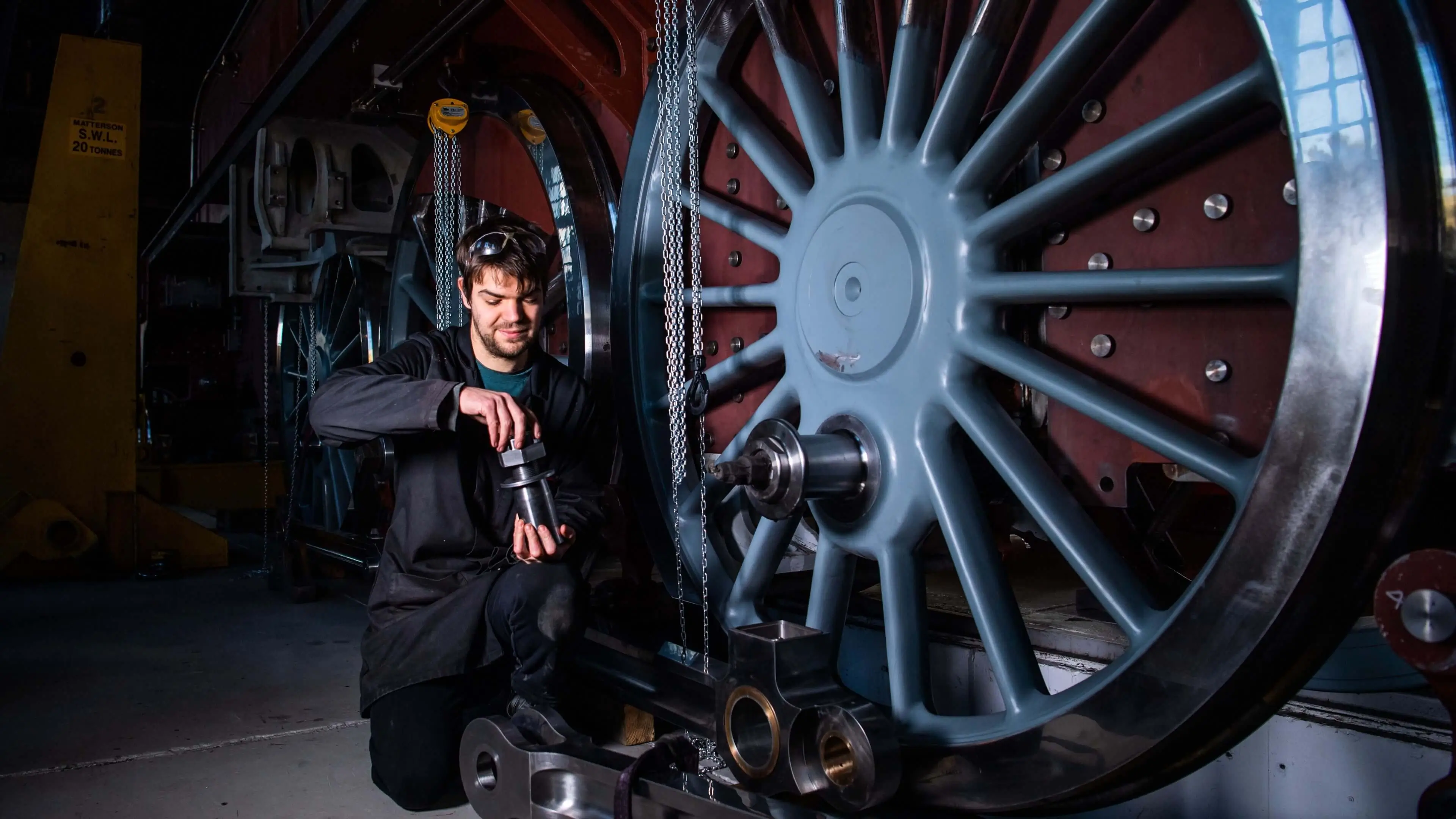 Man holding a large bolt and crouching in front of a large locomotive wheel
