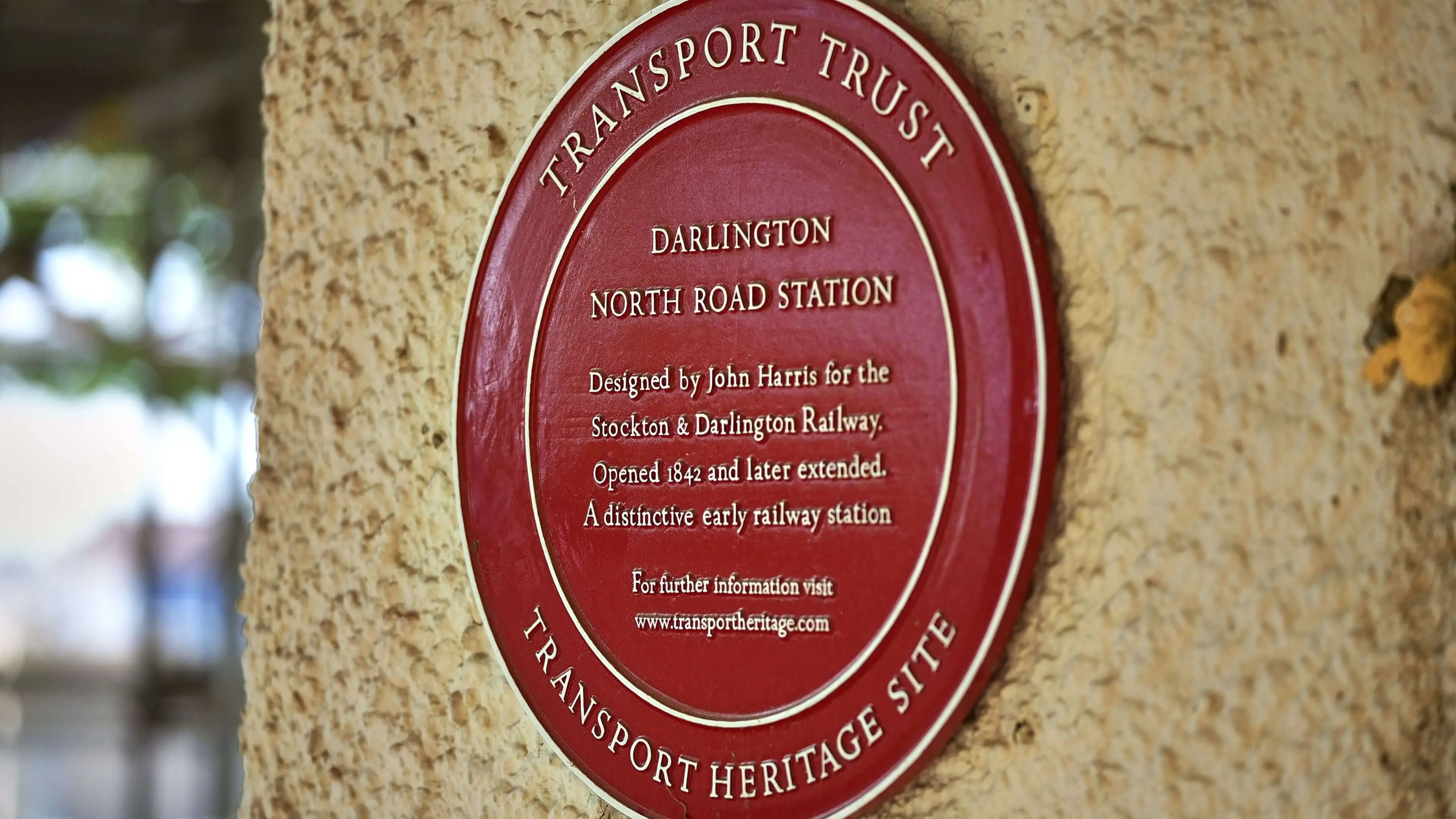 A round, red wall plaque commemorating the Stockton & Darlington Railway and North Road Station Museum