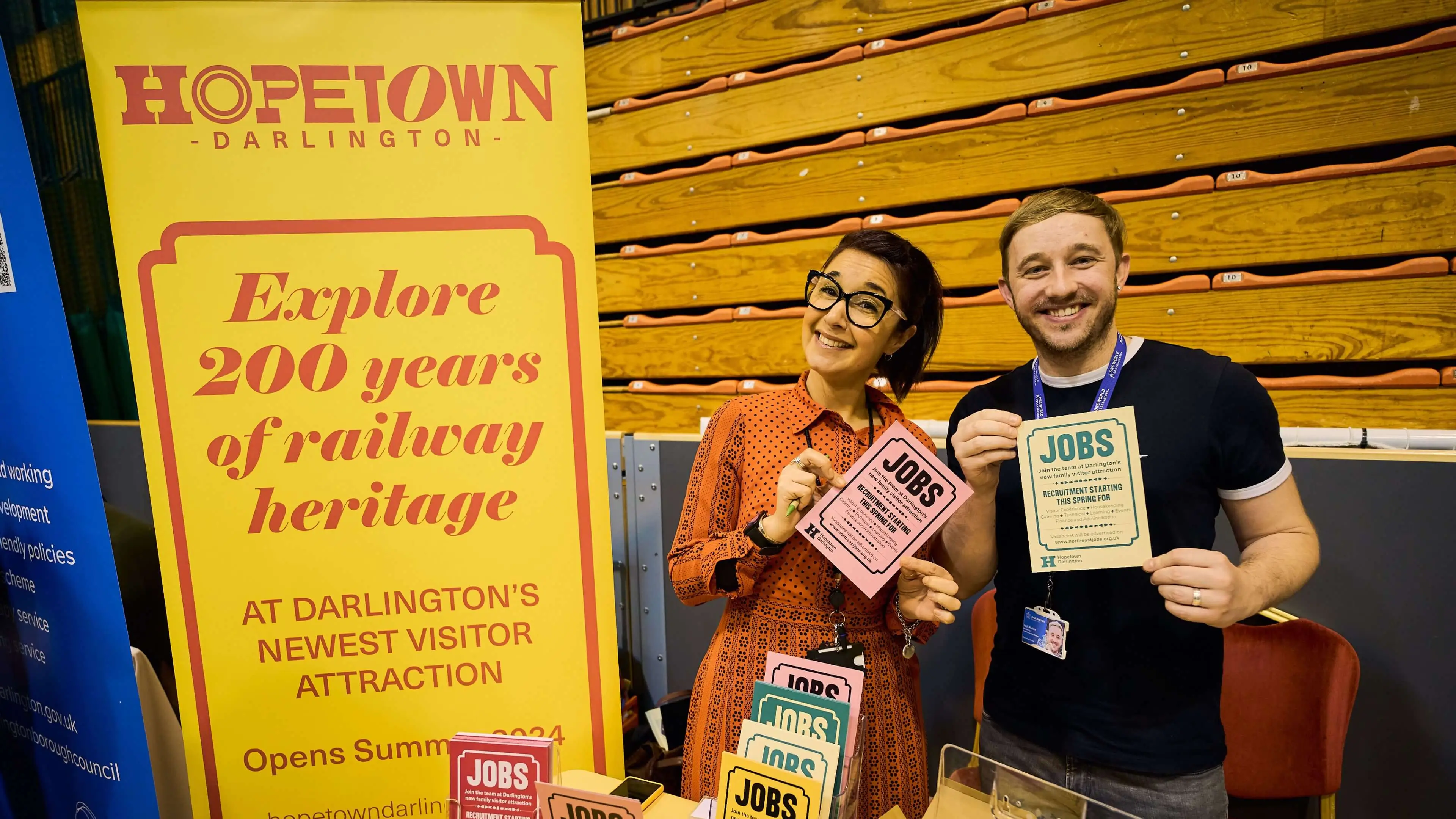 Two people holding multi-coloured Hopetown Darlington branded leaflets 